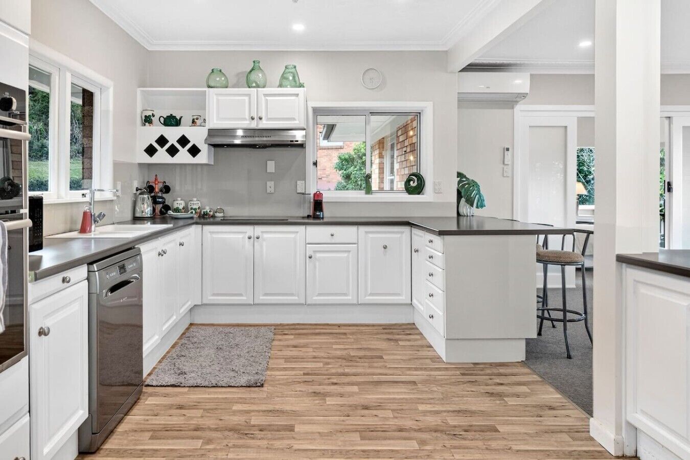 A modern kitchen with white cabinetry, a stainless steel range hood, and a large island with bar stools.