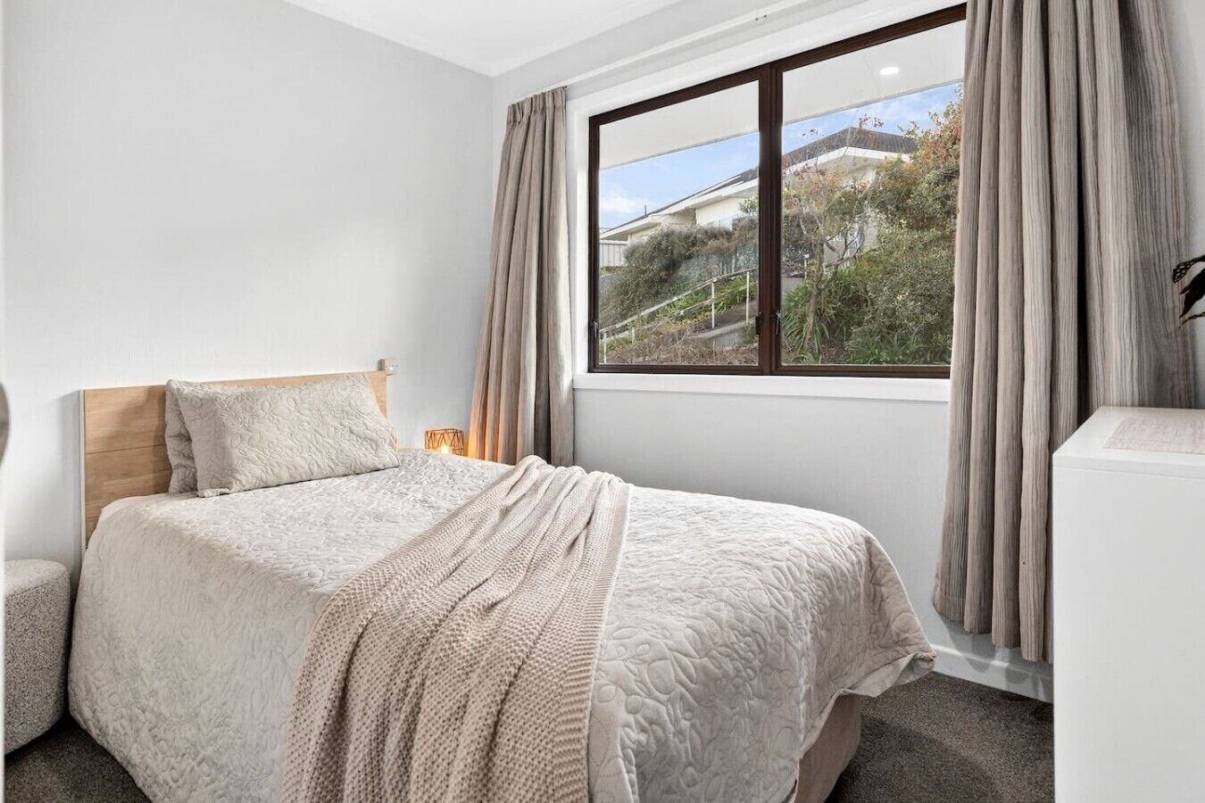 A bedroom with a bed, a bedside table, a lamp, and a window with curtains.