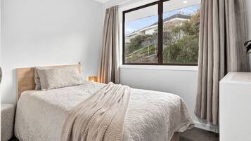 A bedroom with a bed, a bedside table, a lamp, and a window with curtains.