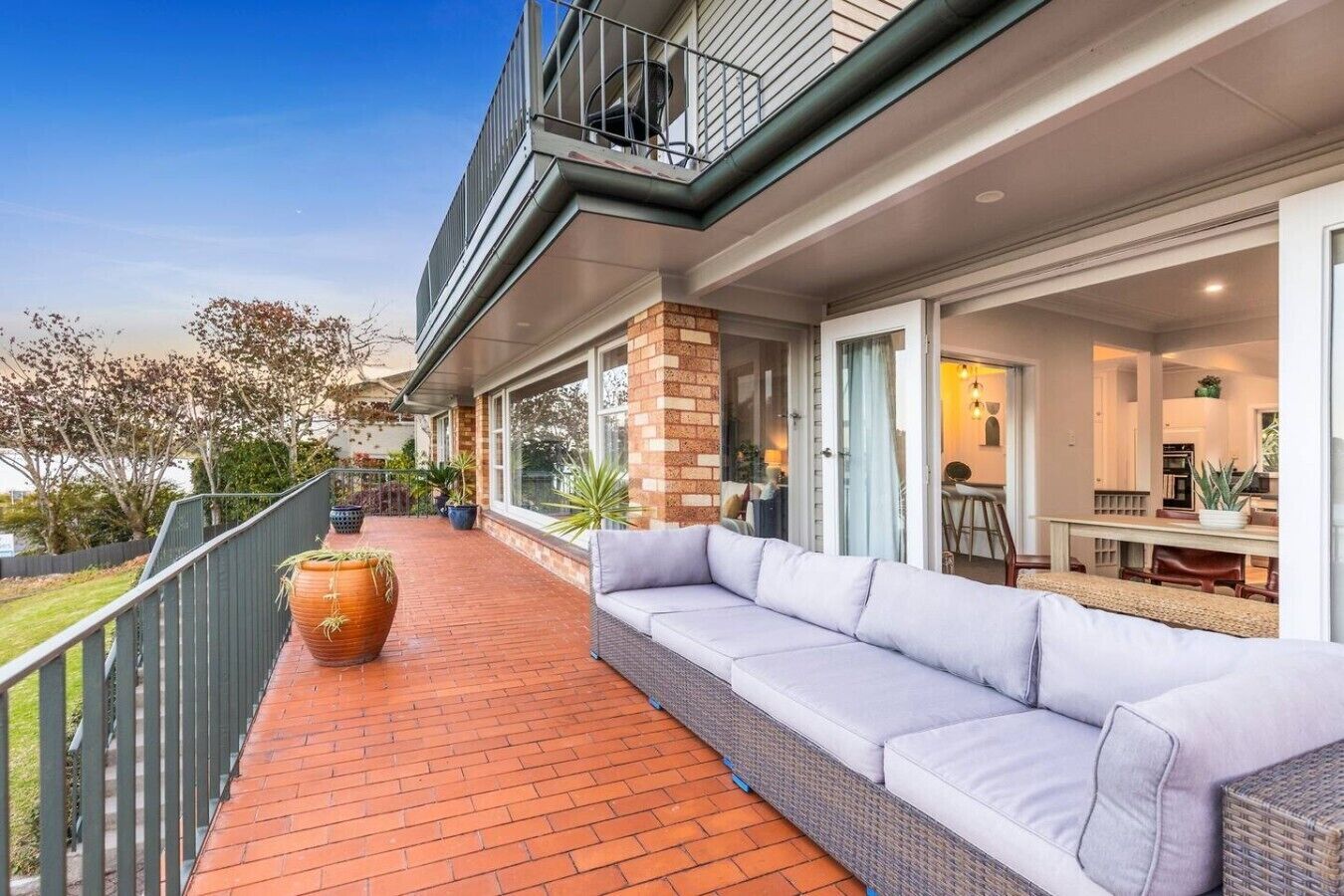 A covered outdoor area with a brick floor, a wicker sofa, and a large terracotta pot.