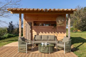 A wooden gazebo with a cushioned sofa and two chairs, a round table, and a fan. - Tranquil French Gîte with Pool, A/C and Stunning Views Near Carcassonne (Raissac-sur-Lampy)