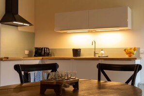 A modern kitchen with a wooden table, two chairs, a coffee maker, and a fruit bowl. - Tranquil French Gîte with Pool, A/C and Stunning Views Near Carcassonne (Raissac-sur-Lampy)