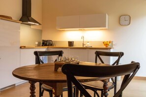 Un'area pranzo con un tavolo rotondo in legno, due sedie, una macchina da caffè e una sveglia appesa al muro.