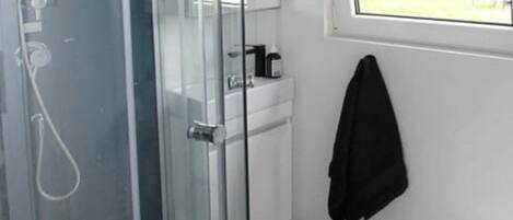 A bathroom with a glass-enclosed shower, a toilet, a sink, and a window with a view of an outdoor area.