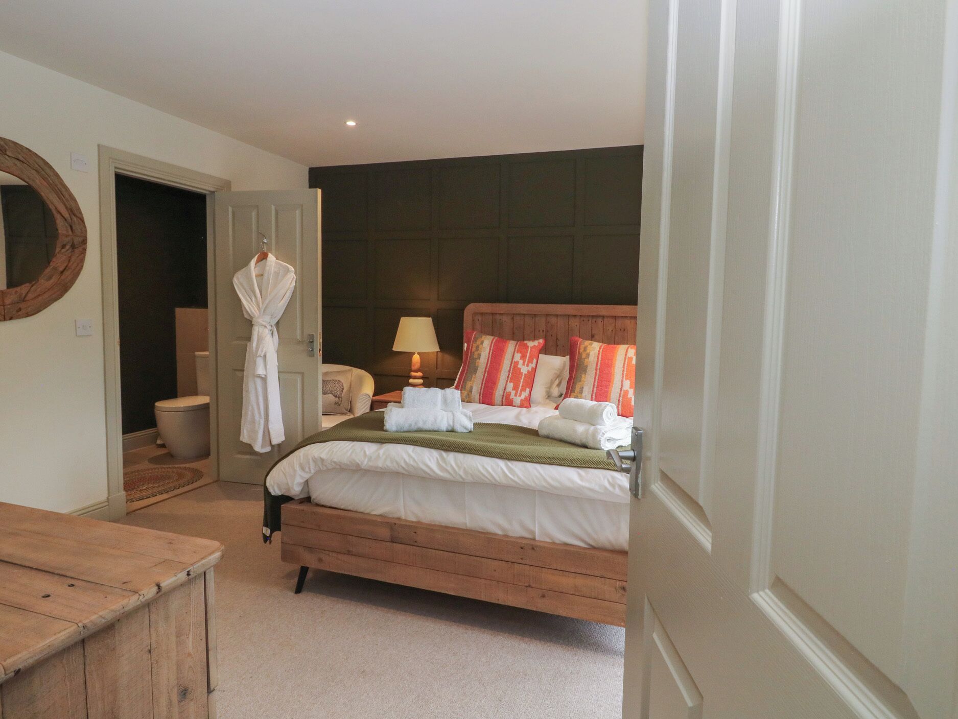Een slaapkamer met een houten bed, een nachtkastje, een lamp en een badjas hangend aan de deur.