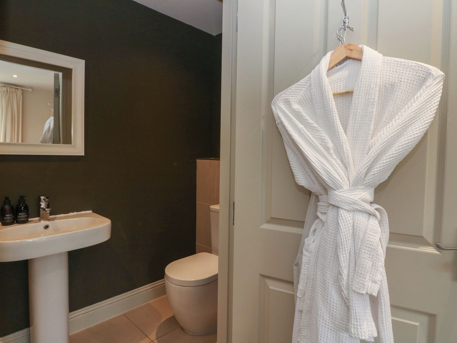 A bathroom with a white sink, a toilet, and a robe hanging on a door.