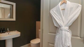 A bathroom with a white sink, a toilet, and a robe hanging on a door.