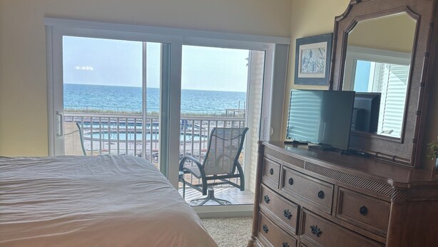 A bedroom with a bed, a dresser, a television, and a balcony with a view of the ocean. - Gulf-front paradise in Springtime on lovely Longboat Key 2/2 -2 pools,pickleball (Longboat Key)