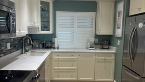 A modern kitchen with white cabinets, a stainless steel refrigerator, and a tiled backsplash. - Gulf-front paradise in Springtime on lovely Longboat Key 2/2 -2 pools,pickleball (Longboat Key)