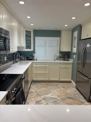 A modern kitchen with white cabinets, a stainless steel refrigerator, and a tiled backsplash. - Gulf-front paradise in Springtime on lovely Longboat Key 2/2 -2 pools,pickleball (Longboat Key)