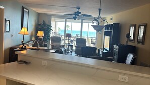 A kitchen with a marble countertop, two stools, a ceiling fan, and a view of the ocean. - Gulf-front paradise in Springtime on lovely Longboat Key 2/2 -2 pools,pickleball (Longboat Key)