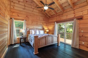 Ein Schlafzimmer in einer Holzhütte mit einem Bett, einem Deckenventilator und Blick durch eine Glastür.