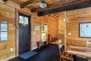 Ein Holzhütten-Interieur mit Holzwänden, einer dunklen Tür, einer Bank, einem Tisch und einer Karte an der Wand.
