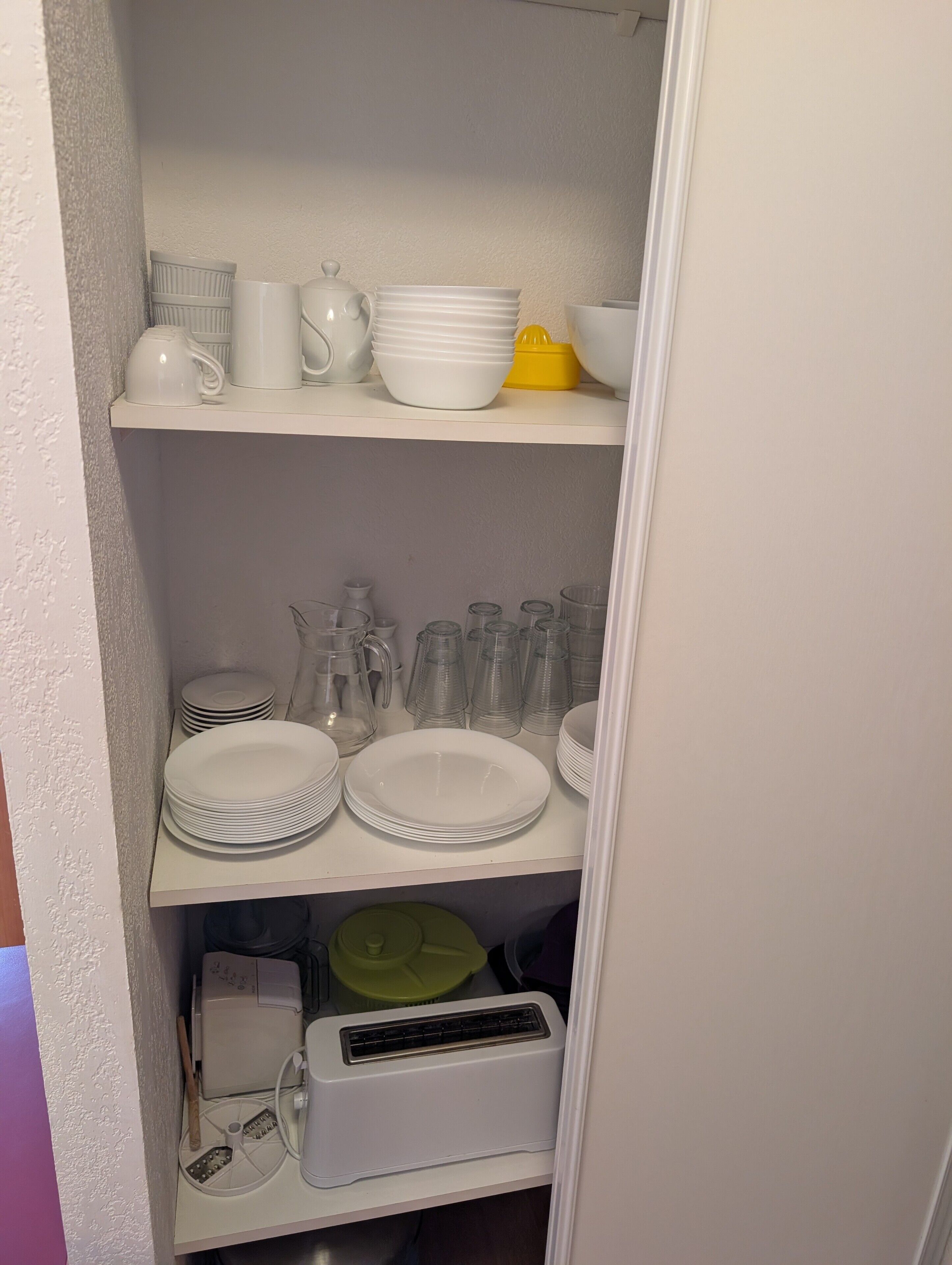 Une cuisine avec des étagères blanches, un récipient vert et un appareil électroménager blanc.