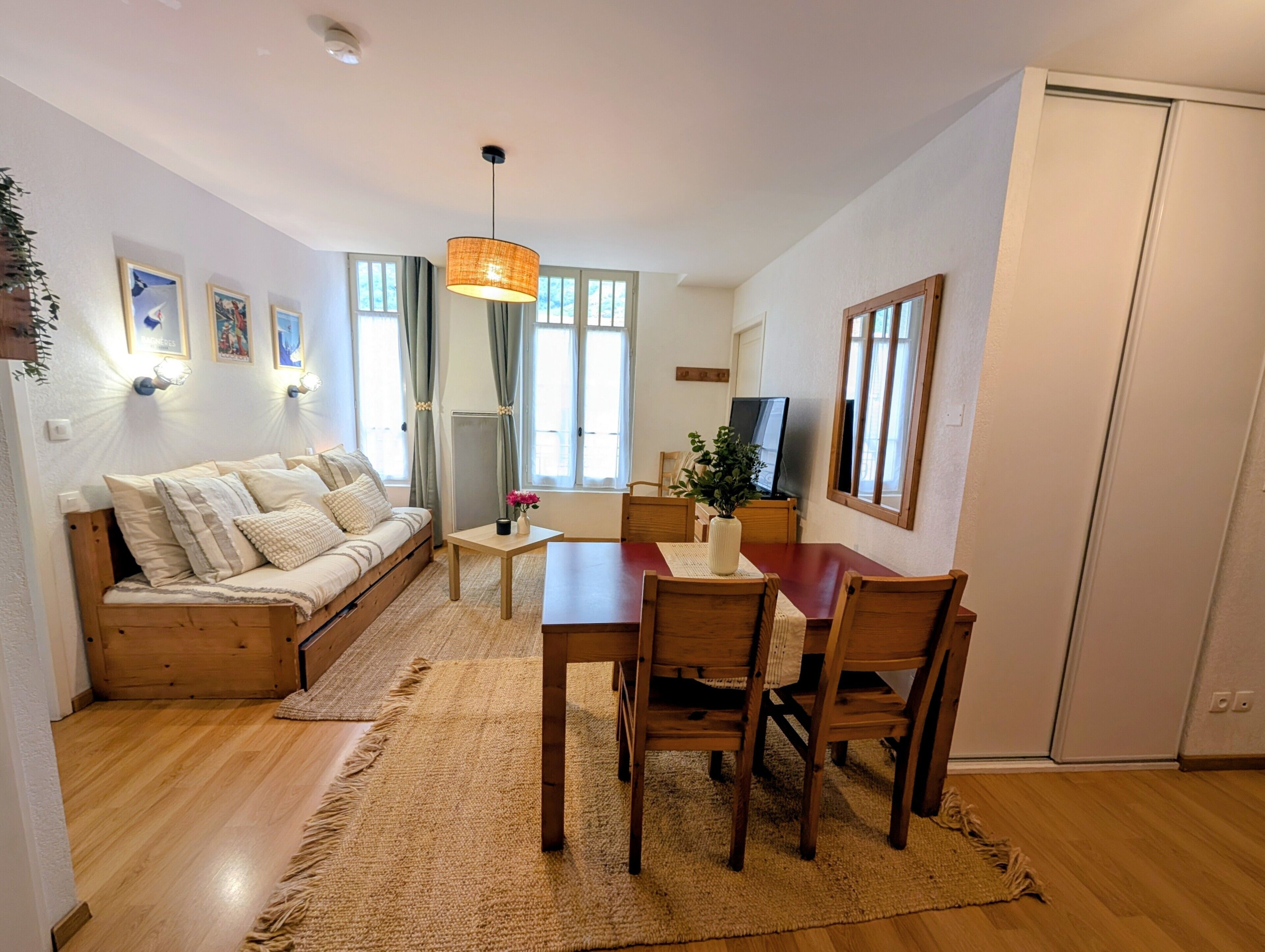 Una sala de estar acogedora con un sofá, una mesa de comedor de madera, sillas, un televisor y un ventanal con cortinas.