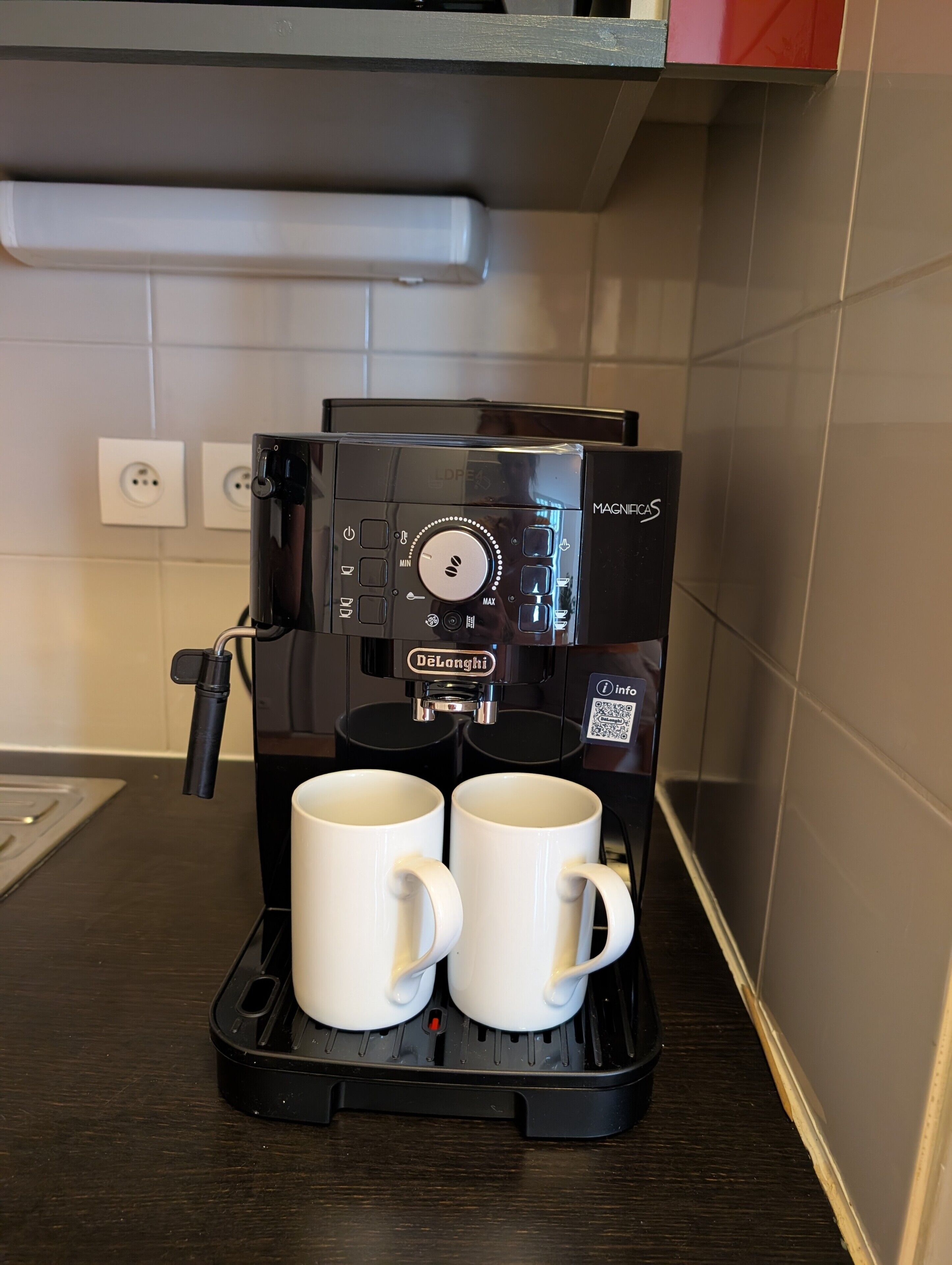 Una màquina de cafè amb dues tasses blanques al calador, damunt d'una cuina.