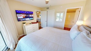 A hotel room with a large bed, a TV mounted on the wall, a dresser, and a door leading to another room. - Great Location Seacrest 315B! (Fort Walton Beach)