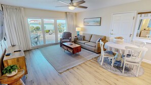A living room with a sofa, coffee table, and chairs, a dining area with a table and chairs, a ceiling fan, and a view through a sliding door to the outside. - Great Location Seacrest 315B! (Fort Walton Beach)