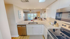 Eine moderne Küche mit Geschirrspüler, weißen Schränken, Granit Arbeitsplatten, einem eingebauten Backofen und einem Deckenventilator.