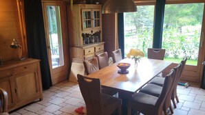 Ein Essbereich mit Holzboden, einem Tisch und Stühlen, einem Schrank mit Glastüren und Blick auf Grünfläche.
