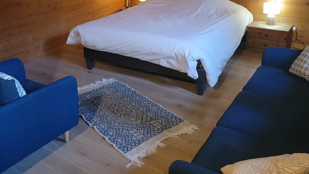 Ein Schlafzimmer einer Holzhütte mit einem Bett, zwei Sofas, einem Teppich und zwei Wandleuchten.