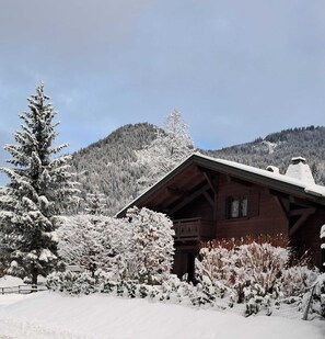 A wooden cabin with a sloped roof, surrounded by snow-covered trees and a mountainous backdrop. - Delightful 5-bedroom chalet in Châtel perfect for your getaway (Châtel)