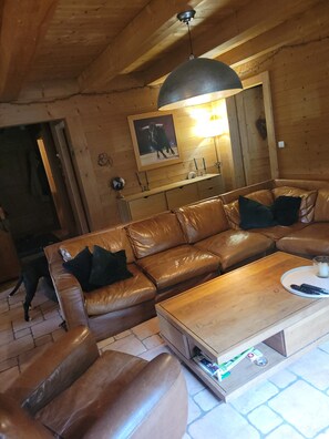 A cozy living room with a leather sofa, a coffee table, and a wooden ceiling. - Delightful 5-bedroom chalet in Châtel perfect for your getaway (Châtel)