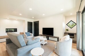 Ein modernes Wohnzimmer mit Sofa, Sesseln, einem Couchtisch, einem Flachbildfernseher und einem Fenster mit Blick.