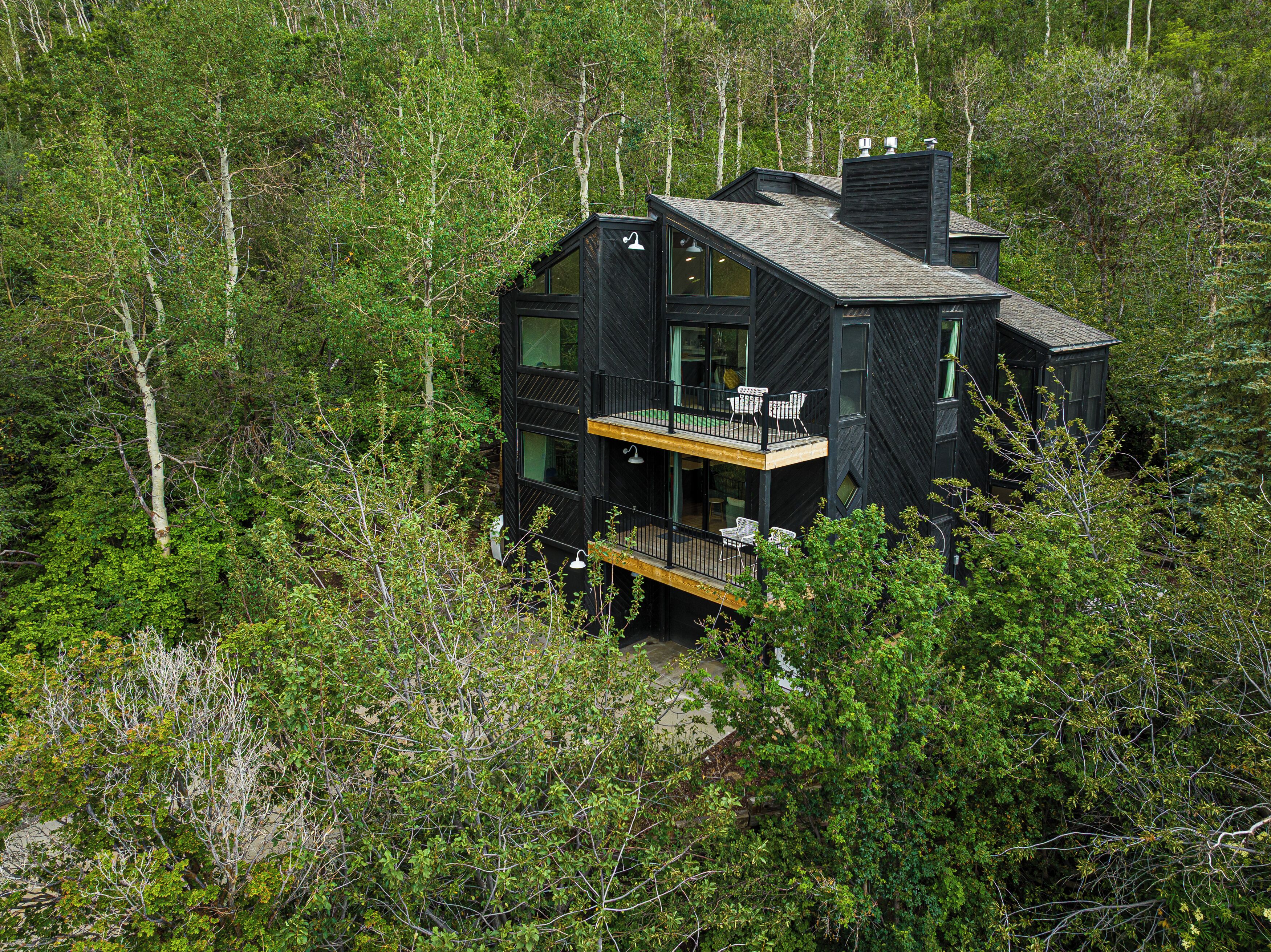 Een modern zwart huis met balkon, omgeven door dicht bos.