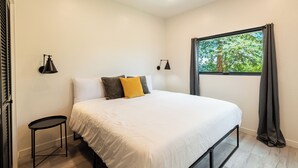 Une chambre à coucher avec un lit, deux tables de chevet, une fenêtre avec des rideaux et des lampes fixées au mur.
