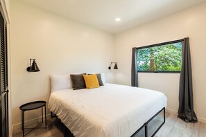 Ein Schlafzimmer mit einem Bett, zwei Nachttischen, einem Vorhangfenster und Wandleuchten.