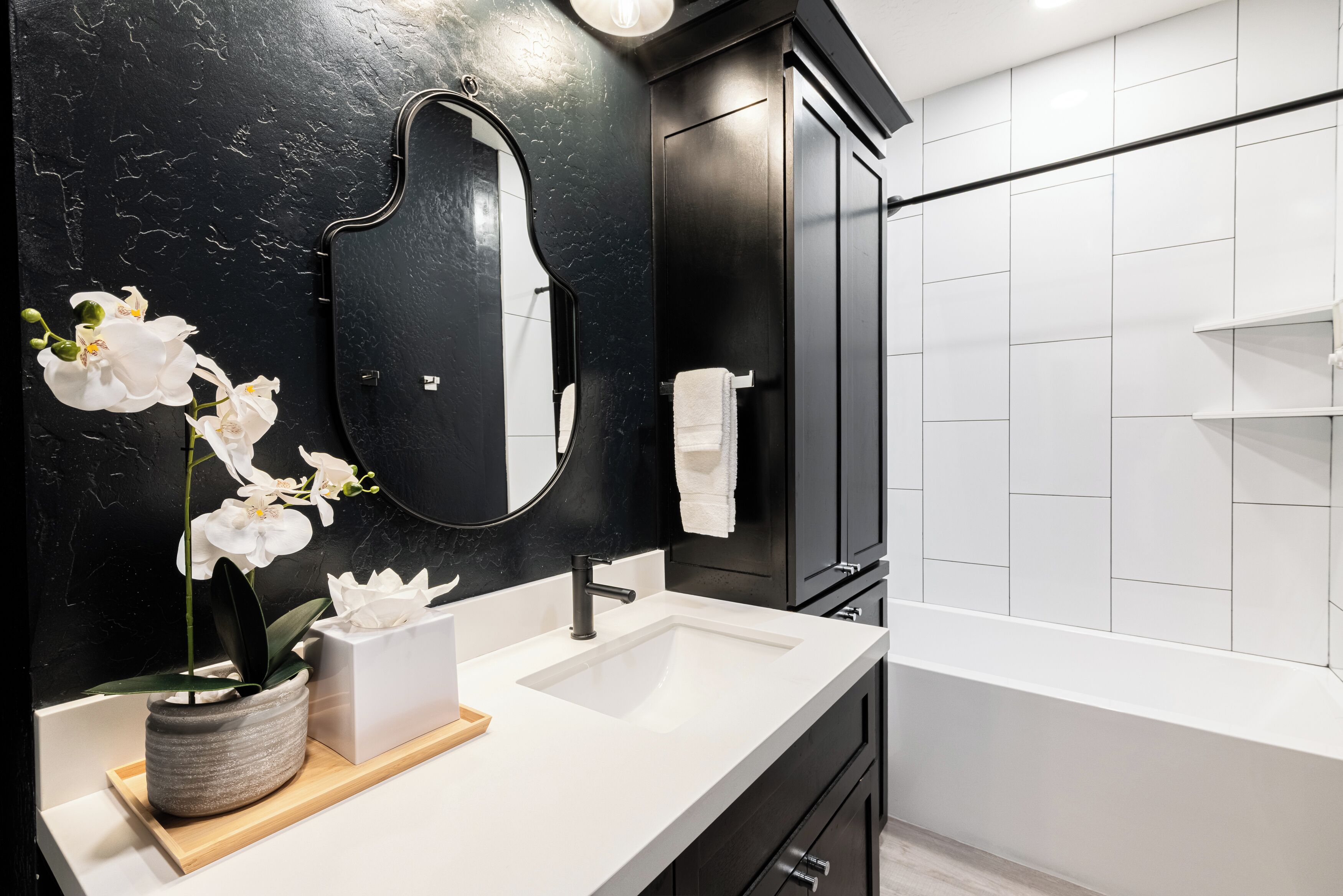 A modern bathroom with a black wall, a white sink, a mirror, and a bathtub.