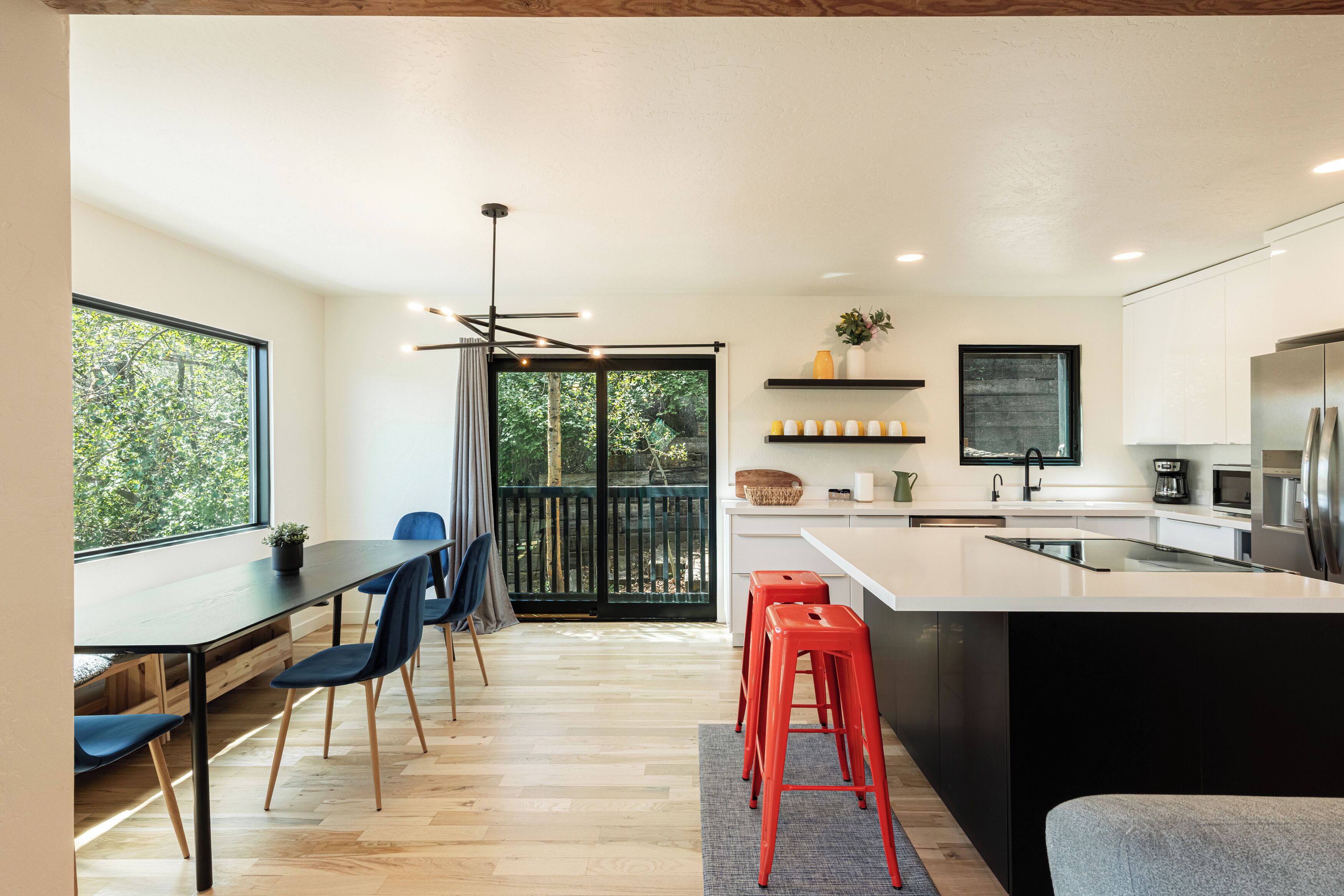A modern kitchen with a large island, wooden flooring, and a dining area with chairs and a table.