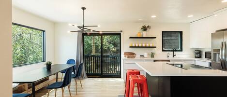 A modern kitchen with a large island, wooden flooring, and a dining area with chairs and a table.