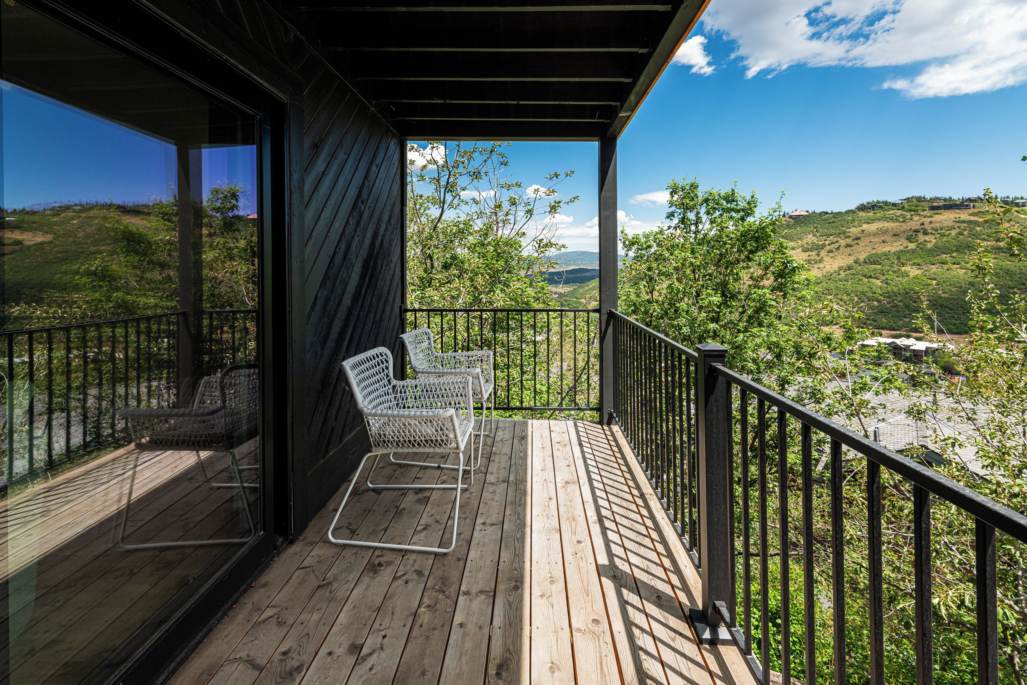 Eine Holzterrasse mit zwei Korbstühlen, mit Blick auf eine hügelige Landschaft mit Bäumen und blauem Himmel.