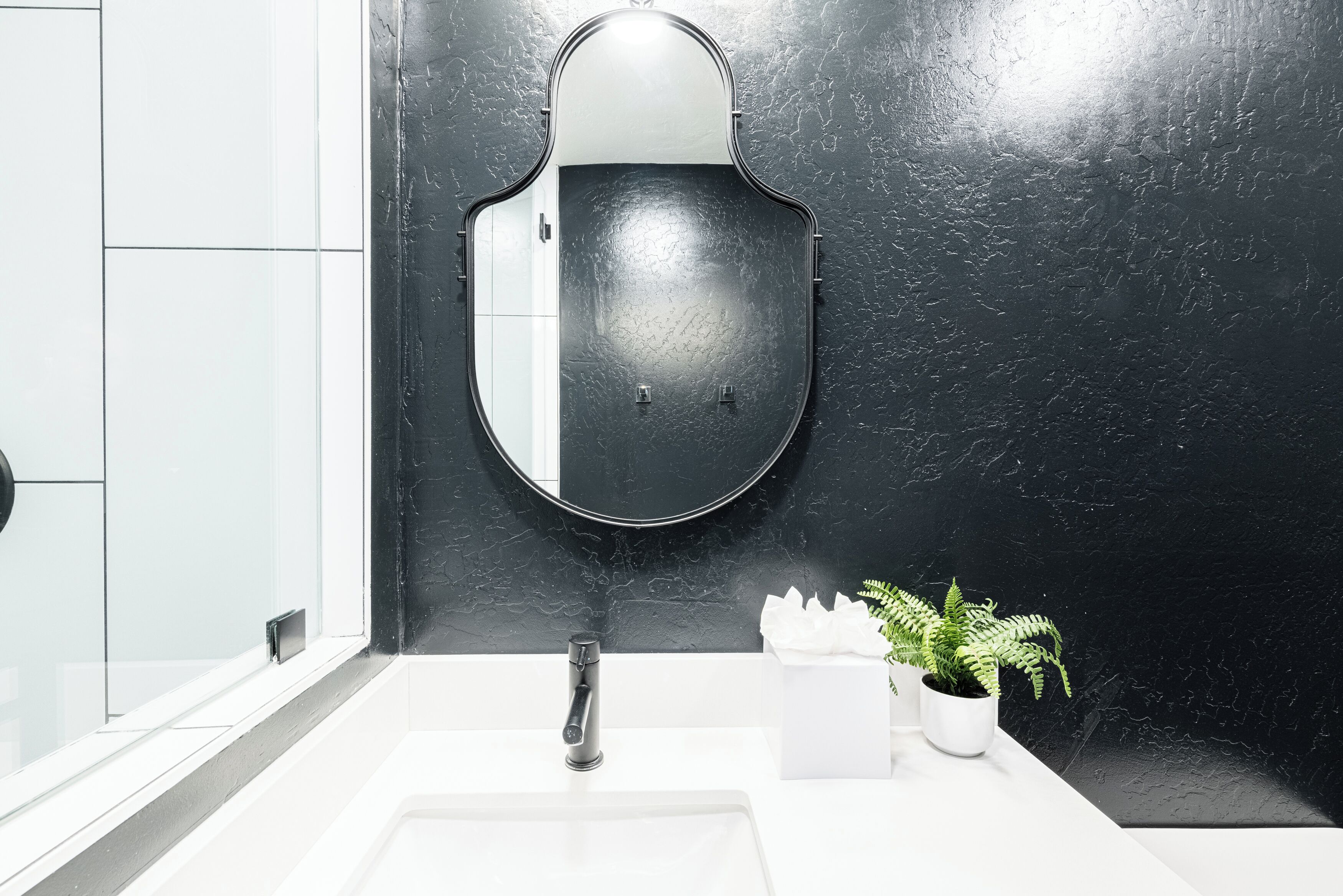 Une salle de bain avec un mur en marbre noir, un lavabo blanc et un miroir.