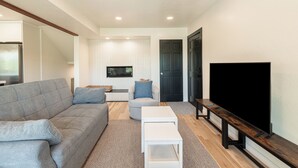 Un salon moderne avec un canapé gris, une table basse blanche, un téléviseur à écran plat et un banc en bois.