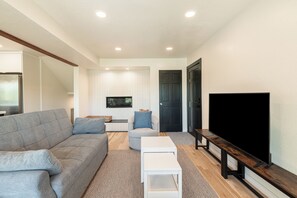 Ein modernes Wohnzimmer mit einem grauen Sofa, einem weißen Couchtisch, einem Flachbildfernseher und einer Holzbank.