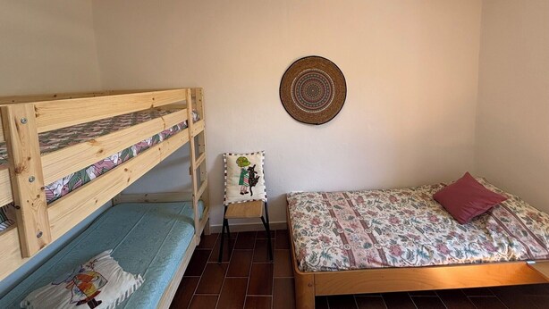Ein Zimmer mit einem Etagenbett, einem Einzelbett, einem kleinen Stuhl und einer Wanddekoration.