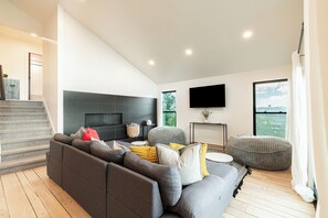 Ein modernes Wohnzimmer mit grauem Sofa, Flachbildfernseher, Kamin und großem Fenster mit Aussicht.
