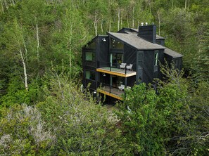 Eine zweistöckige Holzhütte mit Balkon, umgeben von dichtem Wald.