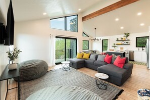 A modern living room with a sectional sofa, a round bean bag, and a dining area with a kitchen in the background. - 2BR mountain-view retreat in Historic Old Town Park City (Park City)