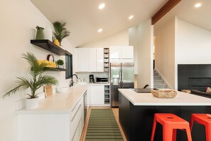 Une cuisine moderne avec des meubles blancs, un réfrigérateur en acier inoxydable, une machine à café et un petit îlot central avec des tabourets.