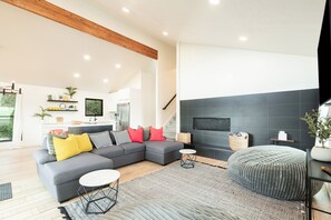 Un salon moderne avec un canapé d’angle gris, une table basse ronde et un pouf gris.