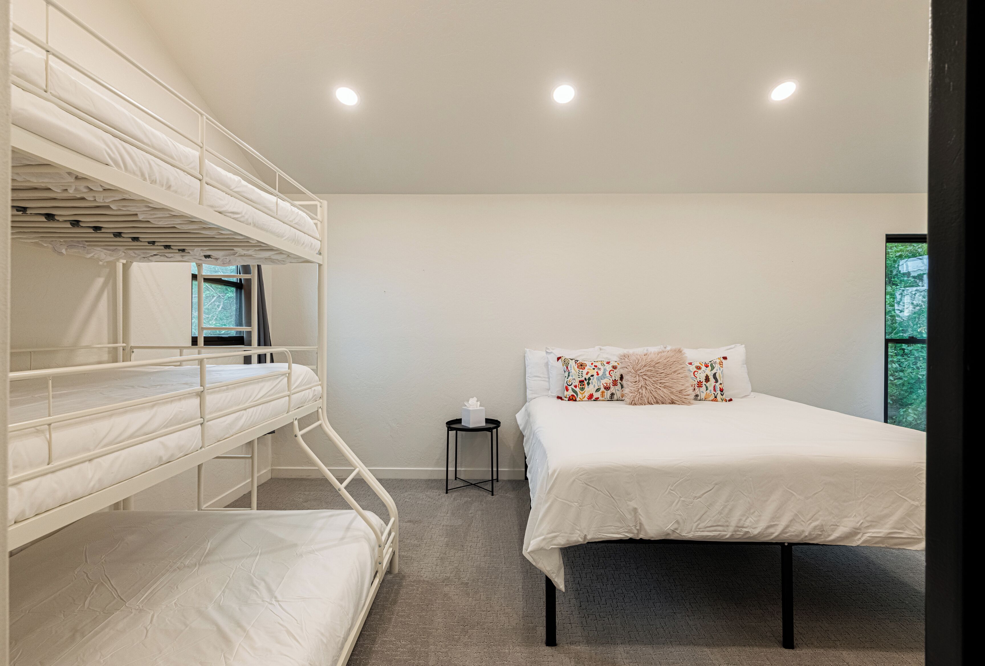 A bunk bed room with a single bed, a small table, and a window.