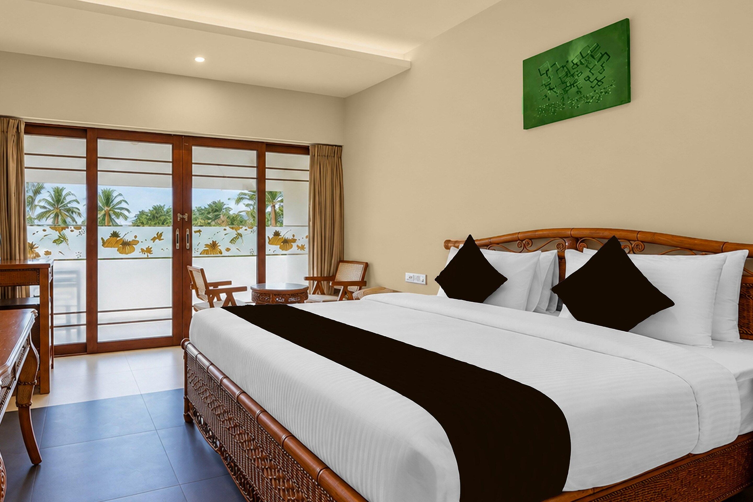 A hotel room with a large bed, a desk, chairs, and a view of palm trees through the glass doors.