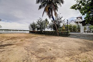 A dry, open area with a palm tree, a hedge, and a building with a white facade and a sloped roof. - Suite With Sea View Palette Sealine (Kochi)
