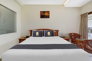 A hotel room with a bed, two pillows, a bedside table with a phone, a chair, a table, and a painting on the wall. - Suite With Sea View Palette Sealine (Kochi)