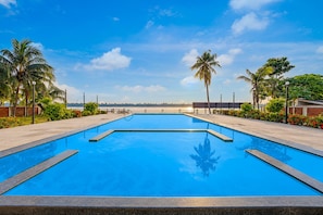 Una piscina rectangular con agua azul cristalina, rodeada por una solana empedrada y palmeras.