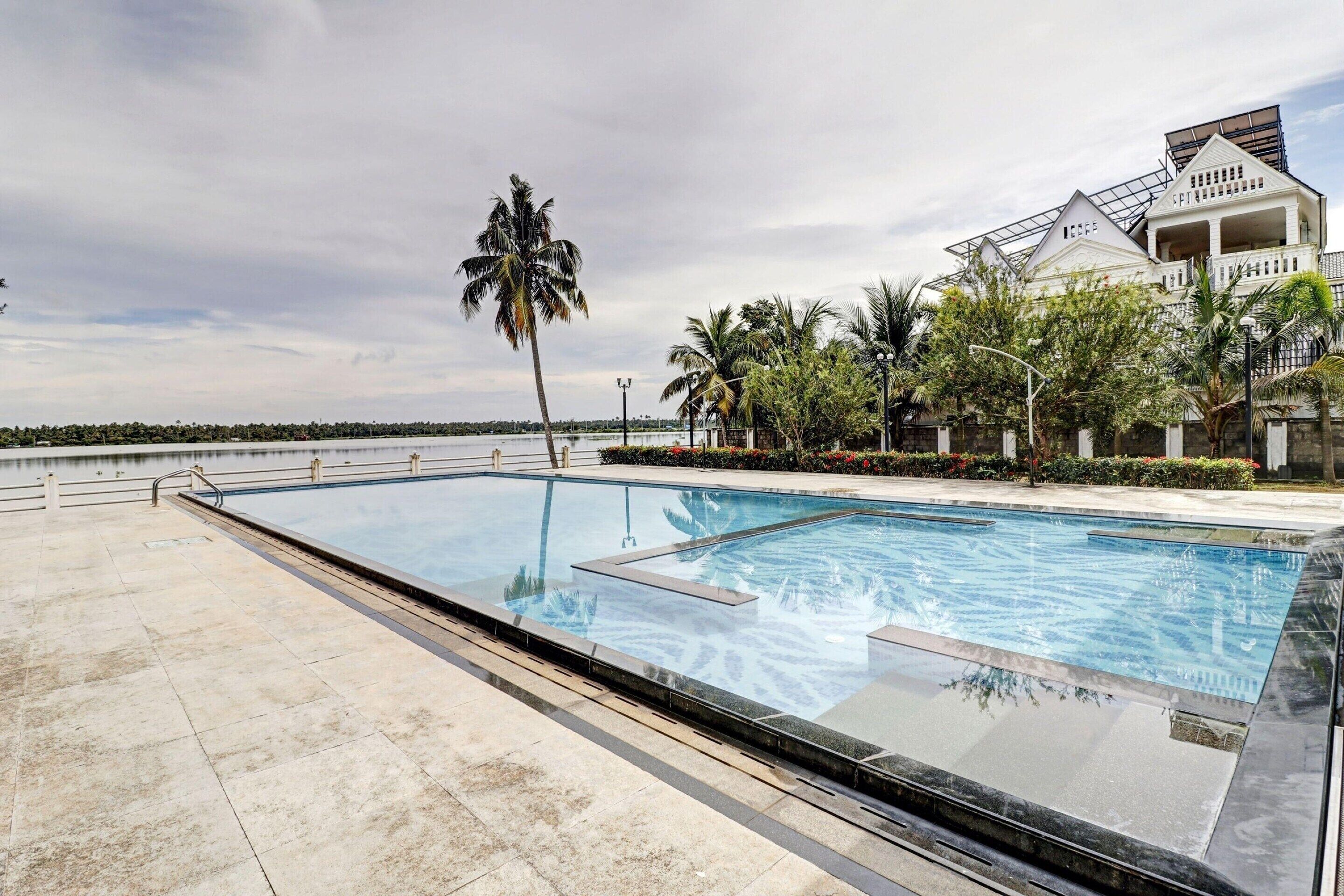 Una piscina con vista despejada al mar, rodeada de palmeras y un edificio con balcón.